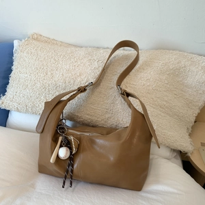 Brown leather hobo tote bag with creative baseball charms on a soft minimalist background