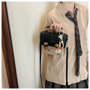 Detail of black ostrich-textured crossbody bag with golden hardware and playful duck charm