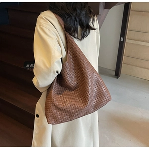 Detail of woven texture on a large brown leather tote bag worn by a model in soft light