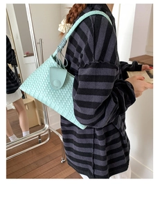 Side view of mint green woven shoulder bag with magnetic flap worn by a model
