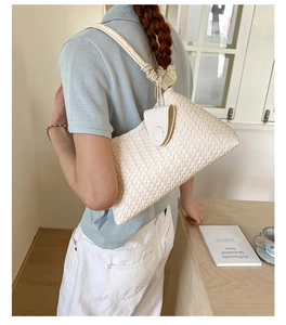Detail of cream woven shoulder bag featuring textured faux leather and a knotted strap buckle