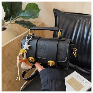 Close-up of black ostrich texture handbag with gold hardware and creative charm pendants