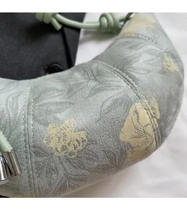 Close-up of light green croissant bag featuring floral print and knotted shoulder strap