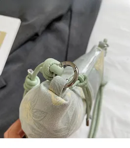 Detail of light green printed bag showing silver carabiner hardware and woven rope strap