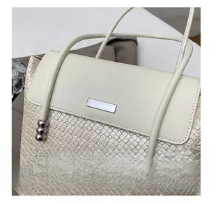Detail of beige woven tote bag featuring silver decorative beads and metal clasp