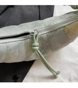 Detail of silver zipper and knotted leather pull on light green quilted floral bag