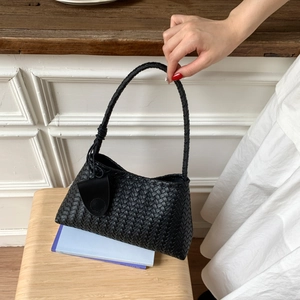 Detail of black woven leather underarm bag with classic intrecciato texture on wood chair