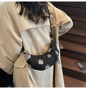Close-up of black crescent dumpling bag with floral patterns on a stylish model