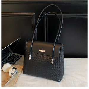 Close-up of black woven leather shoulder bag detail with silver hardware and laptop
