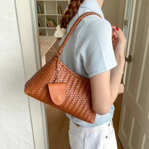 Detail of woven brown leather shoulder bag with circular pendant shown on a model