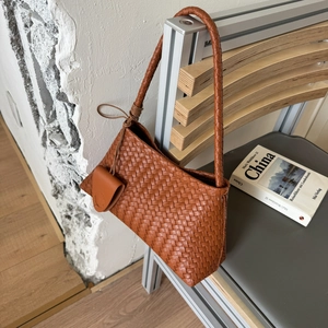 Detail of a brown woven leather underarm bag with a matching mini pouch on a modern chair