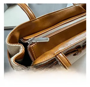 Detail of silver zipper closure on canvas tote with brown leather trim and stitching