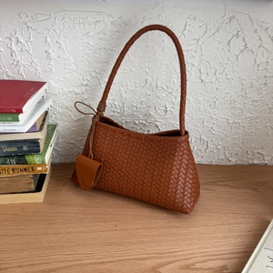Detail of a brown woven leather hobo bag with a knotted handle and matching mini pouch