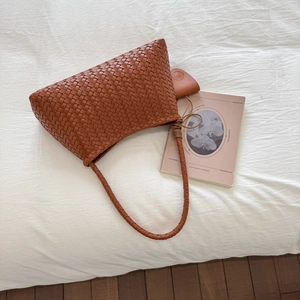 Detail of a brown woven shoulder bag featuring a knotted strap on white fabric
