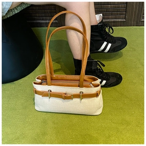 Detail view of canvas handbag with brown leather straps and gold metal buckle accents