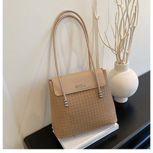 Detail of light brown woven shoulder bag with silver metal trim on a minimalist setup