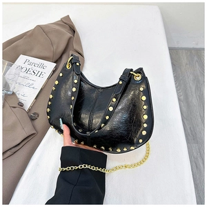 Detail of black glossy faux leather handbag with gold rivets and chain strap accents
