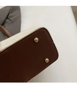 Detail view of woven canvas tote bag bottom with protective gold metal rivets and brown leather