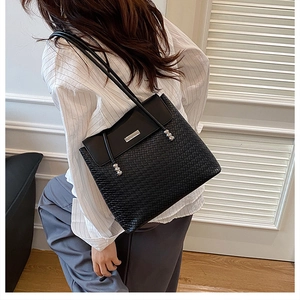 Detail of a black crossbody bag with woven texture base and metallic accent on the flap