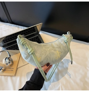 Detail of mint green crescent bag with floral patterns and a knotted strap on a desk