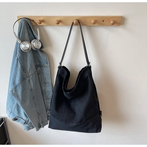 Dettaglio di borsa tote in tela nera minimalista appesa a un gancio con giacca di jeans e cuffie