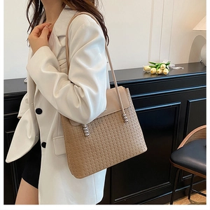 Detail of a beige woven crossbody bag with metallic ball clasp worn with white blazer