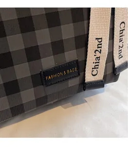 Detail der karierten Umhängetasche mit Leder-Logo-Patch und gewebtem Trageriemen