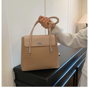 Detail of woven texture and beige flap on a tan tote bag with stylish metallic accents