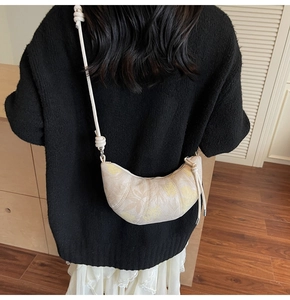 Close-up of beige floral crescent bag with zipper and decorative knotted strap details