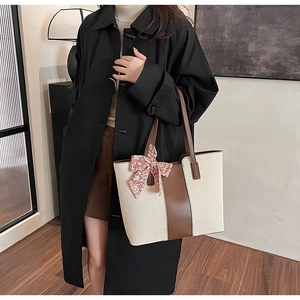 Detail of a large canvas tote bag with brown leather trim and patterned silk scarf handle