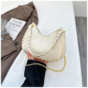 Close-up of cream crescent handbag featuring gold rivets and elegant metal chain strap