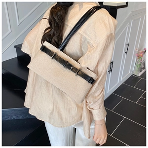 Detail of a beige canvas underarm bag with black leather strap and metal buckle accent
