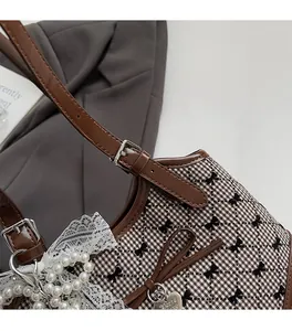 Detail of brown plaid crossbody bucket bag with pearl lace charm and heart pendant