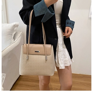 Detail of woven beige shoulder bag with leather flap and dual straps on a model