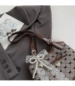 Detail of vintage plaid shoulder bag with lace bow, beads, and heart charm on a blazer
