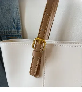 Detail of adjustable brown leather strap with gold buckle on a cream tote bag