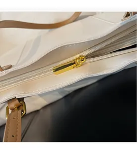 Detail view of smooth golden metal zippers and light brown leather strap on white tote bag