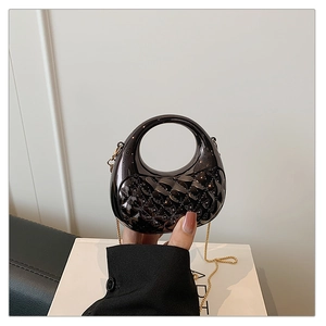 Detail of black patent leather crossbody bag featuring quilted texture and gold chain strap