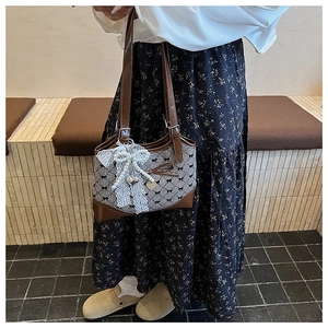 Close-up of retro bucket bag with brown leather, plaid fabric, and lace bow detail