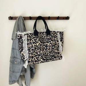 Detailed view of leopard print tote bag with white fringe trim and black woven handles