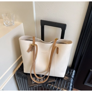 Detail of cream tote bag with brown straps hanging on a suitcase for travel use