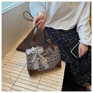 Détail du sac à carreaux vintage avec bordure en cuir marron et pendentif nœud en perle