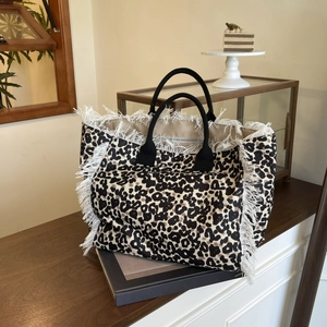 Detail of leopard print tote bag with white tassel trim on a stack of books