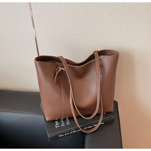 Detail of chocolate brown tote bag with leather texture and golden metal buckle on a sofa