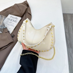 Cream baguette bag with gold studs and metal chain shown in a stylish fashion setting