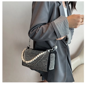 Detail of a black cylinder bag with silver rivets and white pearl chain strap