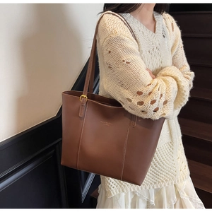 Brown tote bag detail with gold buckle and branding on shoulder, shown on model