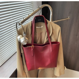 Detailed view of deep red matte leather tote bag styled with a trench coat on a hanger