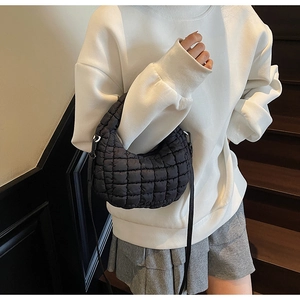 Minimalist black quilted puffy shoulder bag styled with a white sweatshirt and pleated skirt