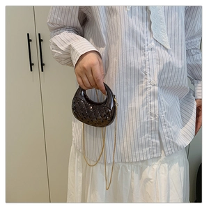 Detail of dark moon-shaped bag with quilted pattern and gold chain on model